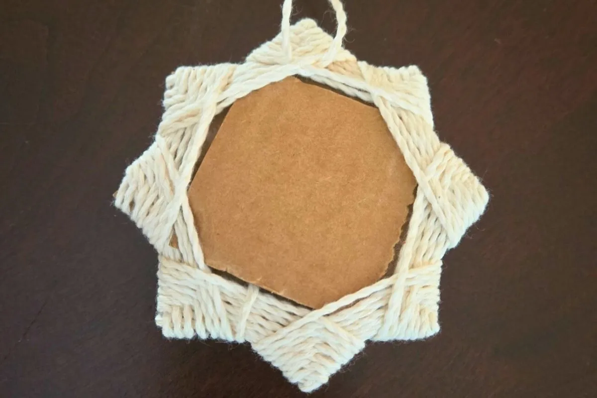 Star-shaped, handmade frame made of woven cream-colored twine around a piece of light brown cardboard.