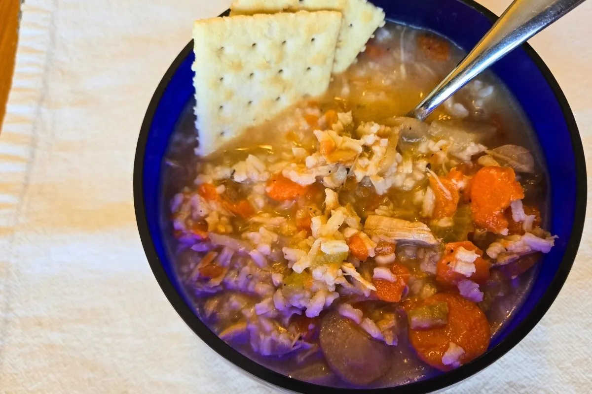 Turkey and rice soup in a blue bowl, topped with crackers, with pieces of chicken, carrots, and rice.