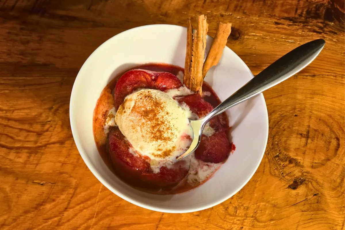 Overhead view of baked plums with melting vanilla ice cream and a sprinkle of cinnamon.