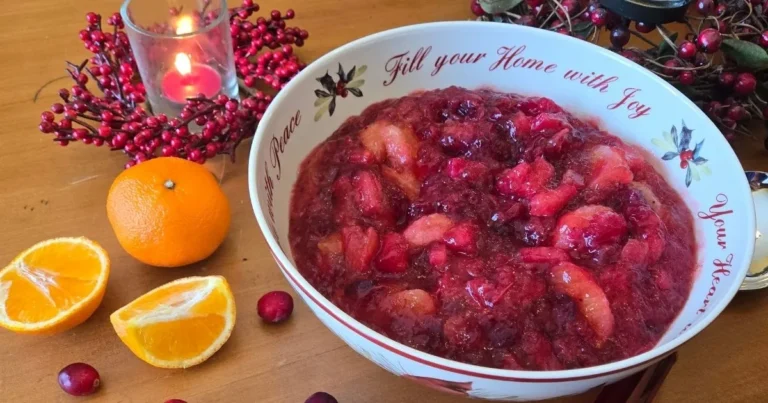 Festive cranberry orange fruit salad served in a holiday bowl on a wooden table with fresh oranges, cranberries, and a lit candle.