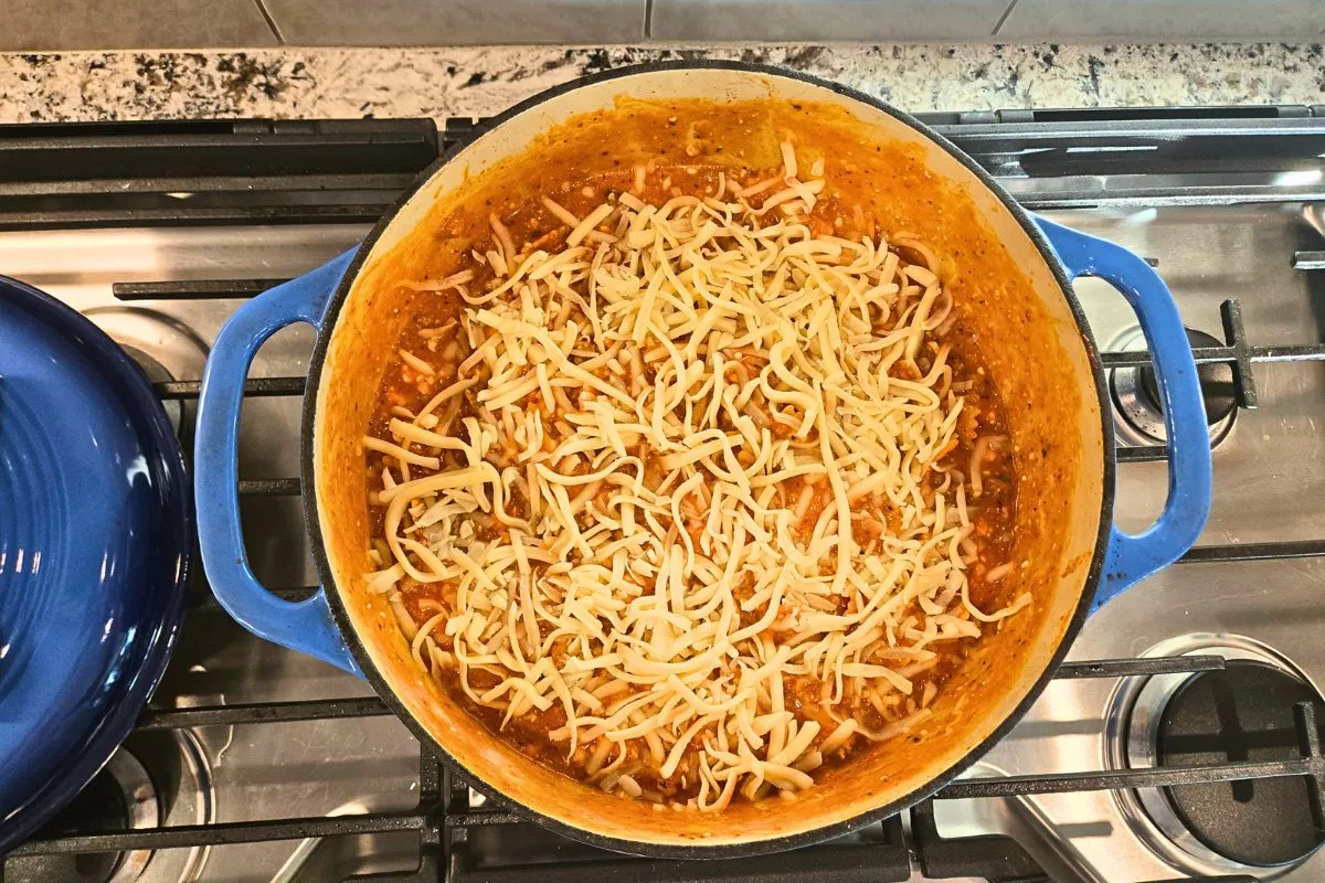 One pot lasagna topped with shredded mozzarella cheese before melting in a blue Dutch oven