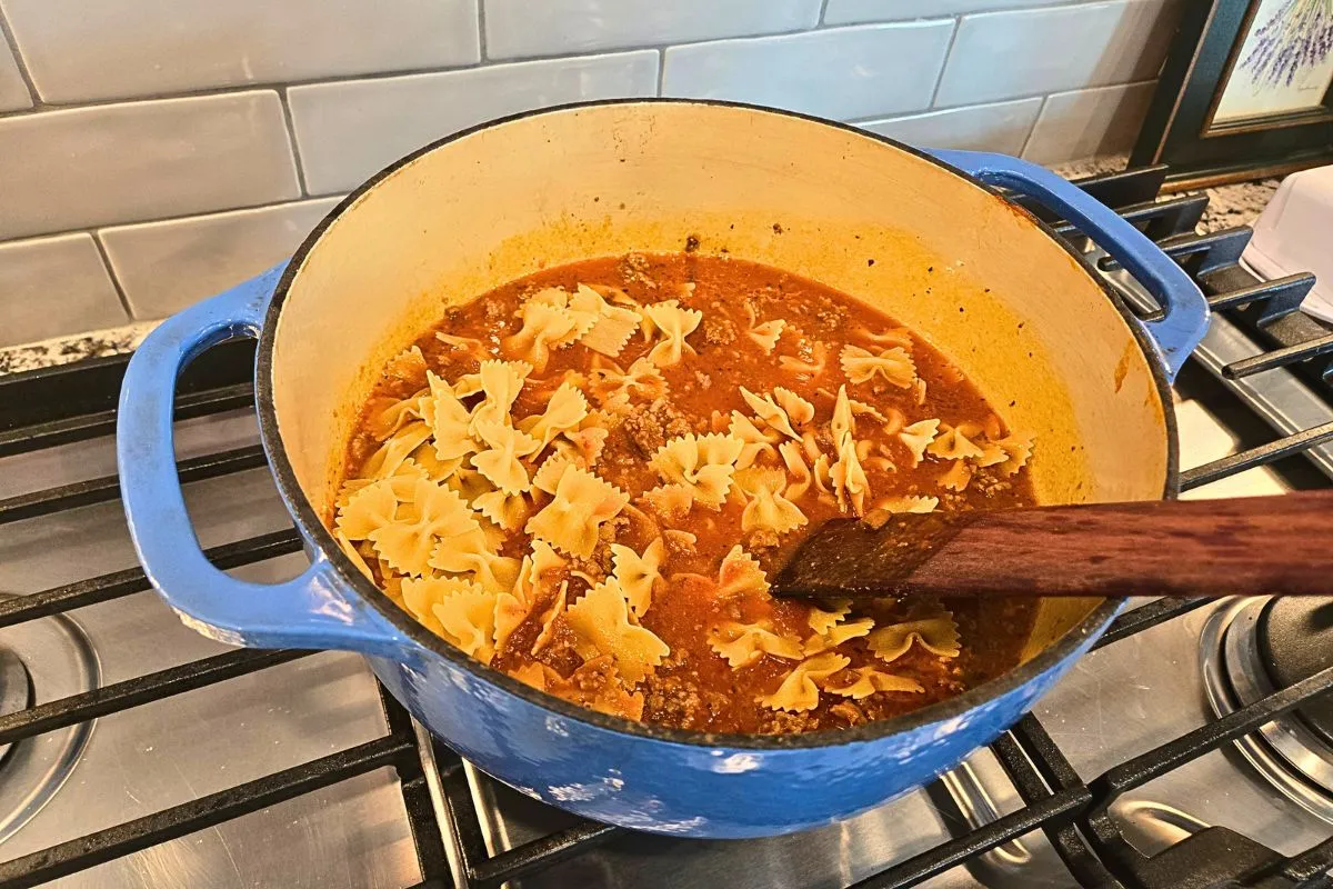 Bowtie pasta simmering in tomato sauce and meat mixture in a blue Dutch oven for easy one pot lasagna