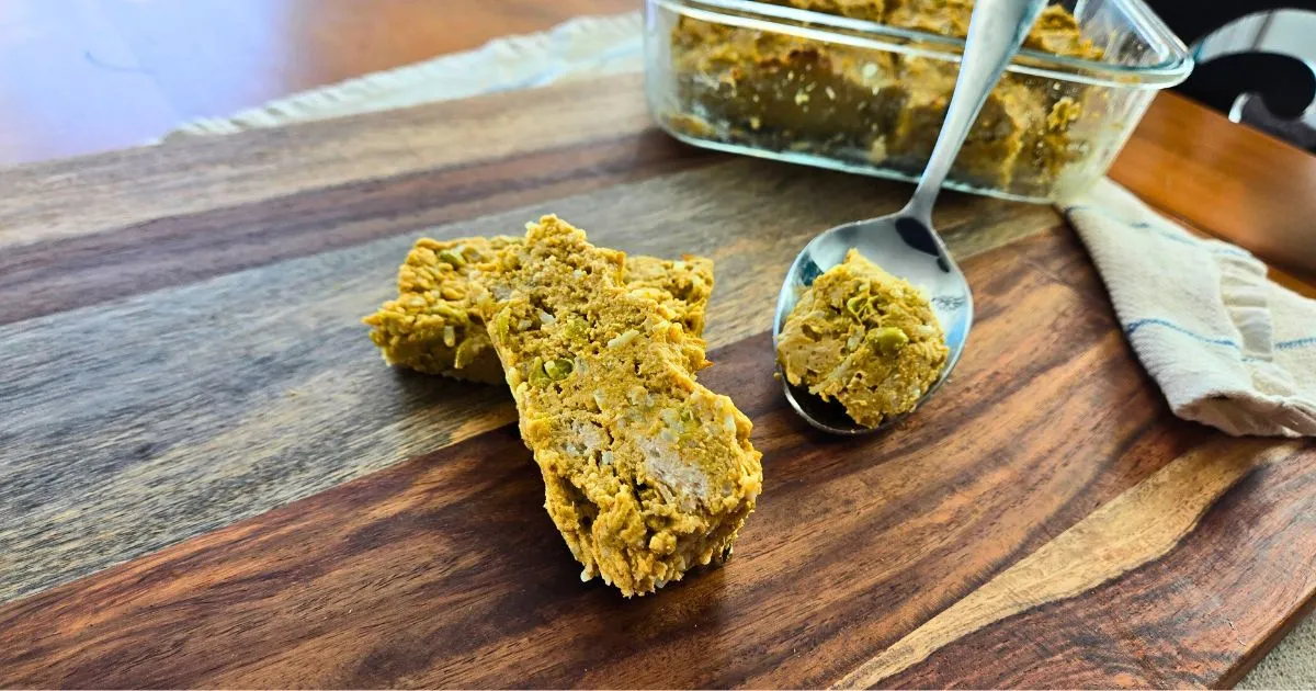 Close-up of homemade dog meatloaf slices with a serving spoon and glass container in the background.