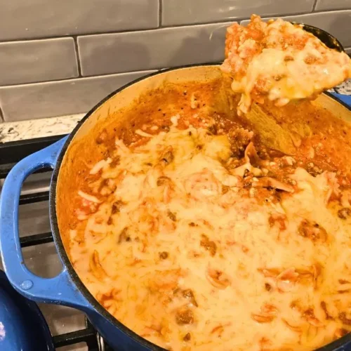 Cheesy one pot lasagna with melted mozzarella and meat sauce being spooned from a blue Dutch oven
