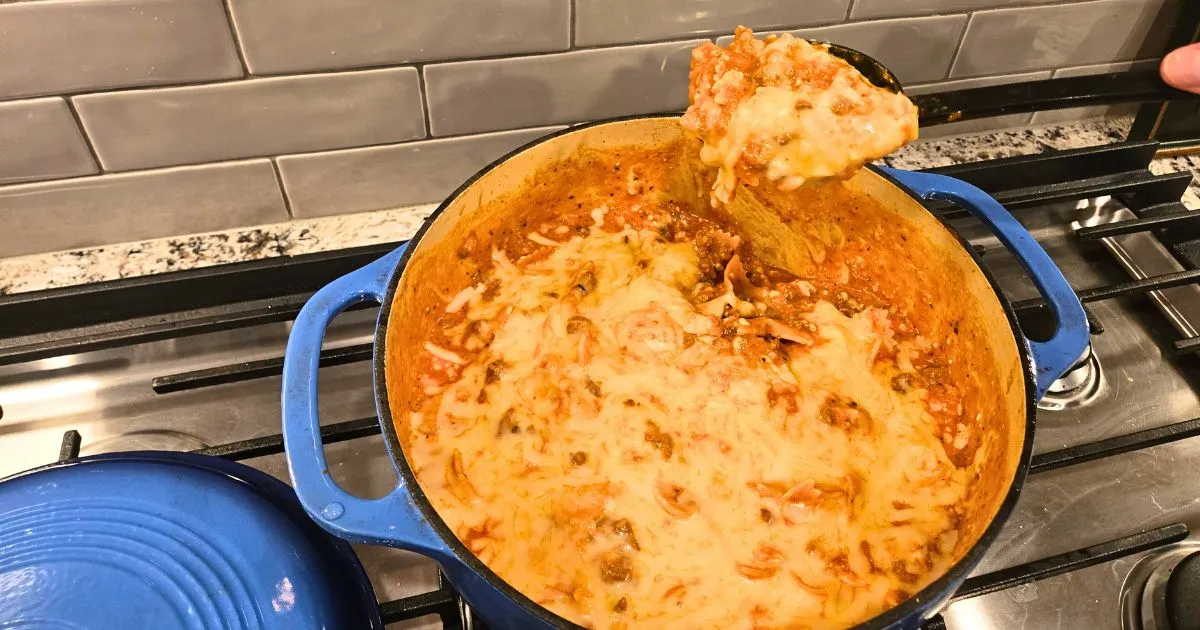 Cheesy one pot lasagna with melted mozzarella and meat sauce being spooned from a blue Dutch oven