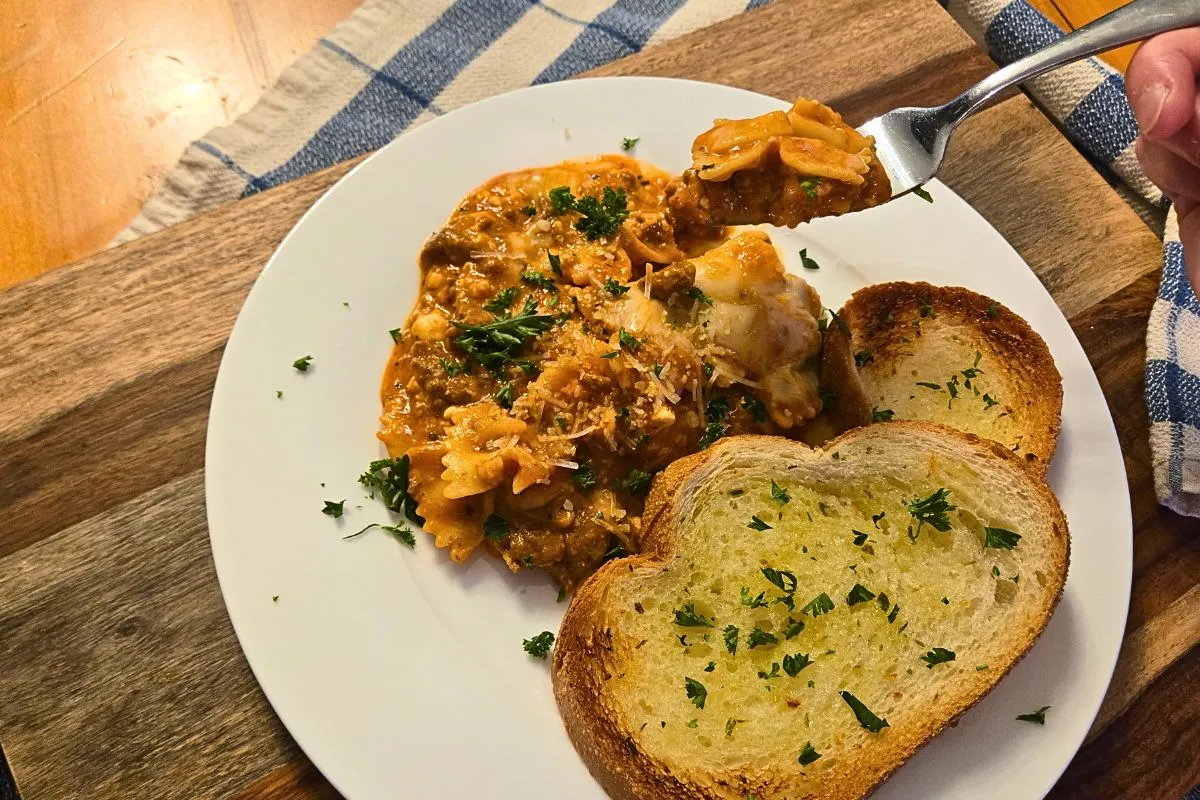 Serving of one pot lasagna with garlic bread and fresh parsley on a white plate for an easy homemade dinner