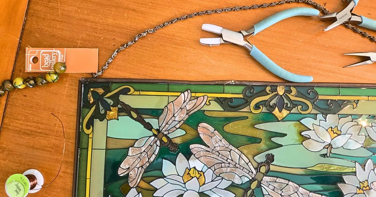 Close-up of faux stained glass window art with jewelry pliers, copper wire, and decorative beads