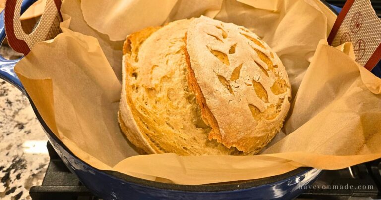 Artisan bread freshly baked in a Dutch oven, showing golden crust and leaf-pattern scoring.